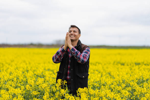 Young attractive Middle Eastern farmer praying in a rapeseed yellow field