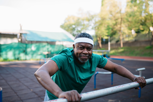 Portrait of an elderly person of colour doing some light exercises and warming up his muscles on an outdoor recreational court