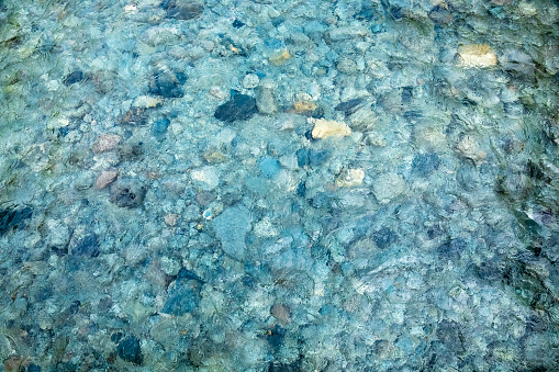 Pebbled riverbed seen through clear rippled turquoise colored water - natural background