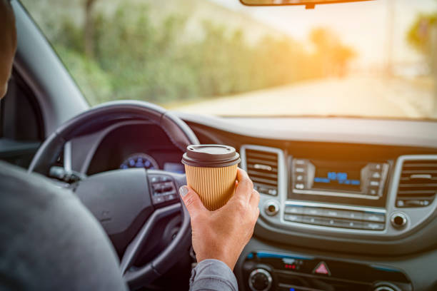 Woman holding disposable coffee cup while driving stock photo