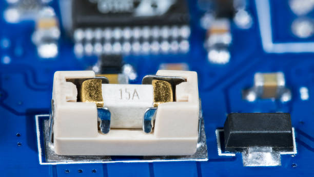 istock Miniature electrical fuse in white holder and black linear fixed voltage regulator on a blue PCB 1394004068