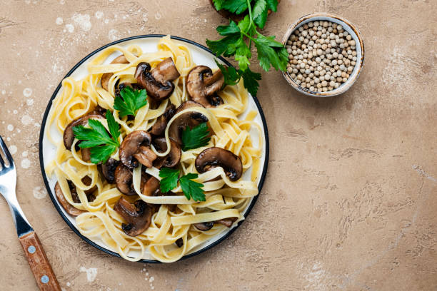 istock Cooked pasta with mushrooms with parsley on plate on beige stone kitchen table background, top view. Vegan cooking and eating, italian cuisine recipe 1394004438