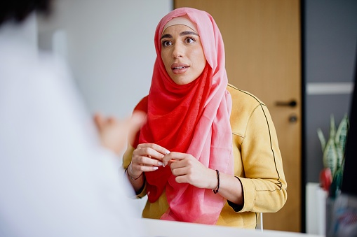 A Muslim woman sits across from her female doctor as she talks with her about cervical cancer