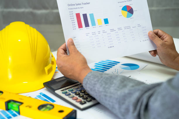 istock Asian engineer with architectural house plan project blueprint, graph and yellow helmet and engineering construction tools. 1394005184