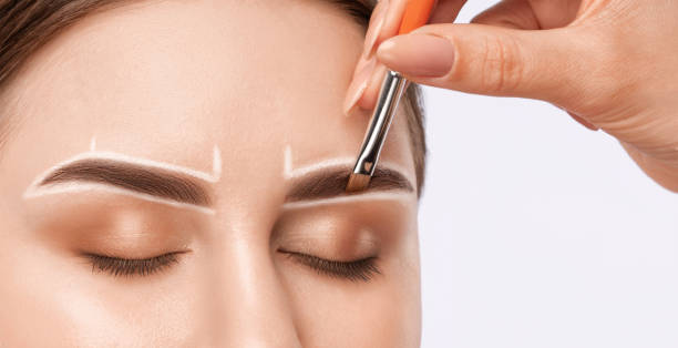 istock Make-up artist makes markings with white pencil for eyebrow and paints eyebrows. Professional makeup and facial care. 1394007070