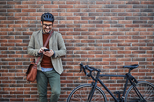 Portrait of a smiling businessman next to his bicycle, an alternative transport, using cellphone