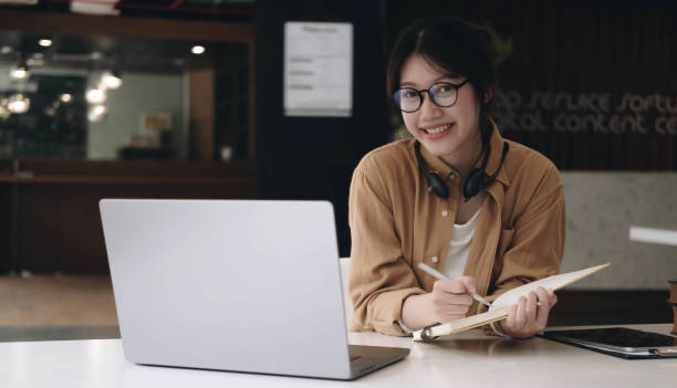 istock Happy asian woman wearing headset make notes talk by conference call doing video chat on laptop in office, smiling chinese support service agent write information consult customer 1394010223