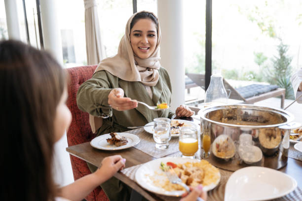 mulher saudita sorridente no final dos anos 20 servindo comida para a filha - saudi arabia child ramadan offspring - fotografias e filmes do acervo
