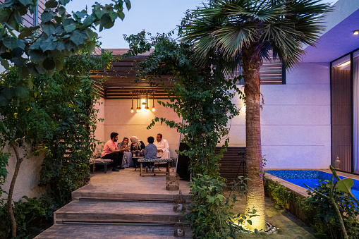 Illuminated modern home exterior with native plant landscaping and Saudi family relaxing in secluded sitting area.