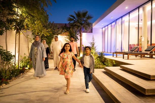 Young Saudi siblings and family outdoors at twilight Full length view of approaching Middle Eastern children in western dress holding hands and smiling at camera with parents and grandparents in background. blue hour twilight stock pictures, royalty-free photos & images
