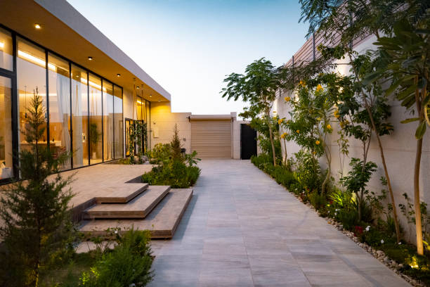 Home exterior at dusk in Riyadh, Saudi Arabia Diminishing perspective outside illuminated modern home with full length glass windows, steps to entrance, and native plant landscaping. courtyard stock pictures, royalty-free photos & images