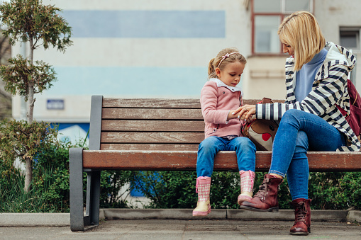 Little girl sitting on park bench with mom after school and having fun