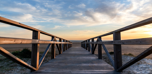 Panoramic view of a wooden walkway leading to the beach at sunset with a beautiful cloudy sky