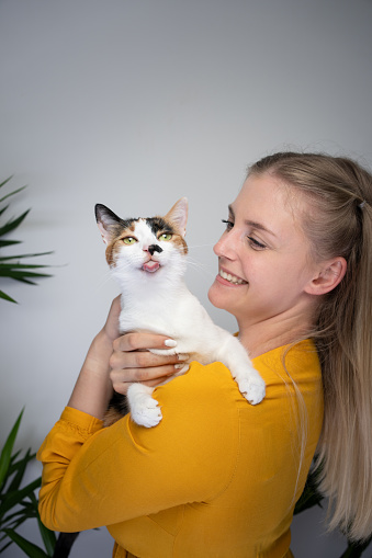 young blond woman carrying her naughty cat that is sticking out tongue looking at camera with copy space