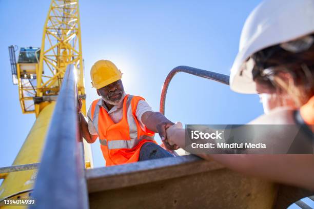 African American Male Cargo Handler Helping Female Coworker To Getting On Harbor Cargo Crane Stock Photo - Download Image Now