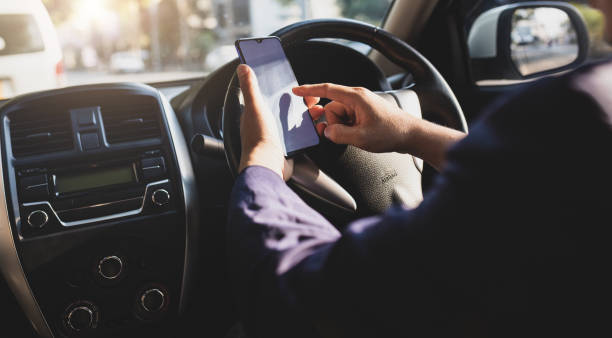 istock Businessman in car typing text on mobile phone to send text message while driving. Man using mobile phone looking at map while driving. Road safety and carelessness concepts. 1394016531