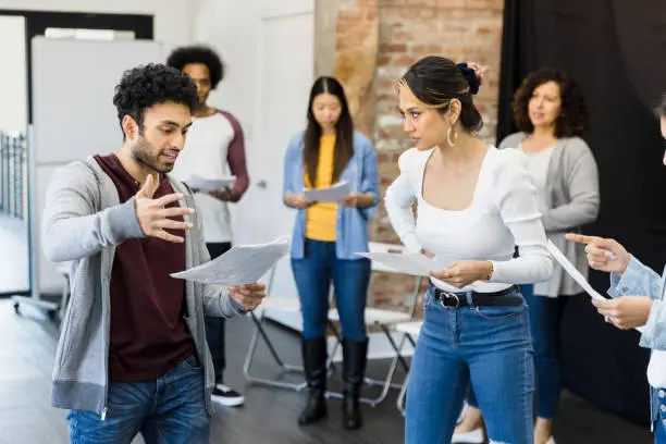 The multiracial group of actors practice the play in the studio.  They each read from a script.