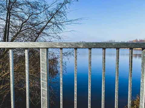 A railing of a bridge over a stream by a lake.