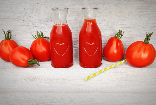 Two bottle of freshness juices on white wooden background with red tomatoes .