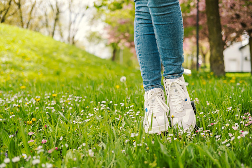Legs of a woman standing on the meadow between flowers.