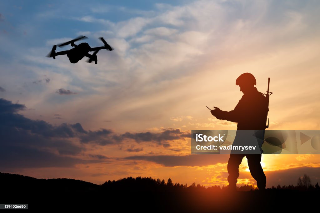 Silhouette of soldier are using drone and laptop computer for scouting during military operation. Silhouette of soldier are using drone and laptop computer for scouting during military operation against the backdrop of a sunset. Greeting card for Veterans Day, Memorial Day, Independence Day. Drone Stock Photo