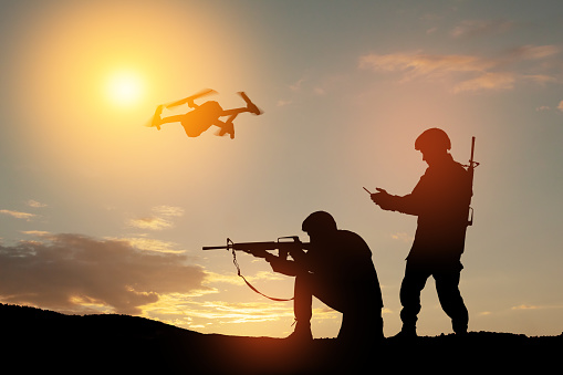 Silhouettes of soldiers are using drone and laptop computer for scouting during military operation.