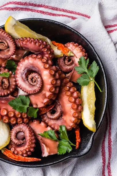 Photo of Grilled octopus, tentacles with herbs, chili, served with lemon on a small pan. Delicious seafood recipes