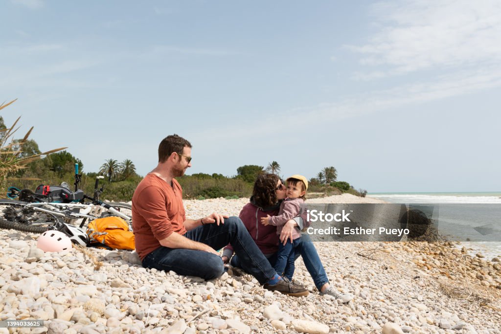 Couple and daugther sitting on a pebble beach with their bikes behind them. Couple and daugther sitting on a pebble beach with their bikes behind them. Sustainable transportation and healthy life. Family Stock Photo