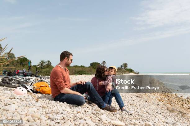 Couple And Daugther Sitting On A Pebble Beach With Their Bikes Behind Them Stock Photo - Download Image Now
