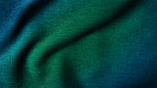 close up texture of creased fabric. gradient in green and blue color tone, woolen fabric. wavy cloth background showing fiber detail. gradient drapery background with beautiful, light and shadow.