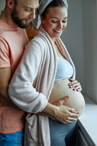 Close up of smiling parents touching pregnant belly at home