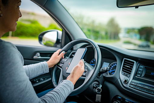Close up view of woman hand holding mobile phone while driving car. Clipping path on mobile screen. High resolution 42Mp outdoors digital capture taken with SONY A7rII and Zeiss Batis 25mm F2.0 lens