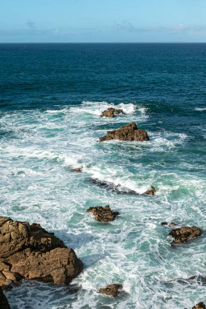 small waves wash around the sharp rocks sticking out of the sea. view of the clear turquoise water of the atlantic and blue sky with some clouds. On the Brittany coast near Crozon, Morgat and Camaret-sur-Mer, Brittany, France