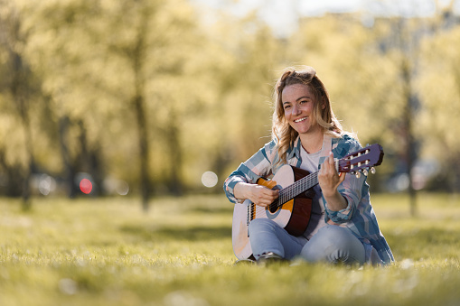 Happy woman sitting on the maedow and playing guitar during spring day