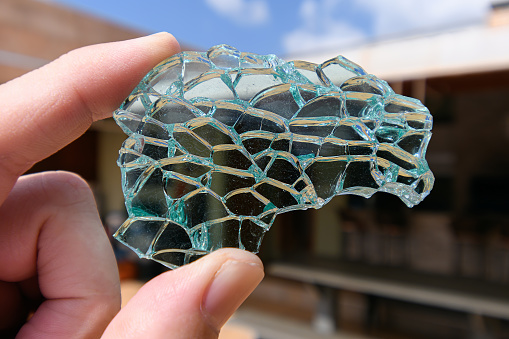 Holding on fingertips a broken piece of tempered glass, green tempered glass. Piece of glass with cracks.