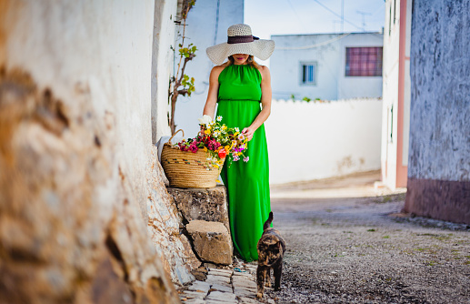 Beautiful woman with a basket of flowers walking the streets of an ancient village in the Algarve with a cat
