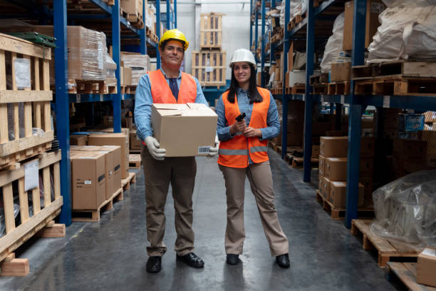 squadra di magazzinieri che sorridono alla telecamera, donna che tiene in mano un lettore di codici a barre mentre l'uomo tiene una scatola - warehouse bar code reader manual worker working foto e immagini stock