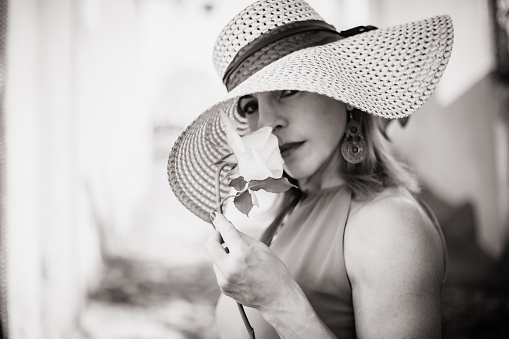 Beautiful and elegant woman with hat smelling the scent of a rose in black & white