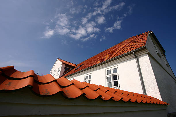 Red weathered roof tiles on a white home under a blue sky stock photo
