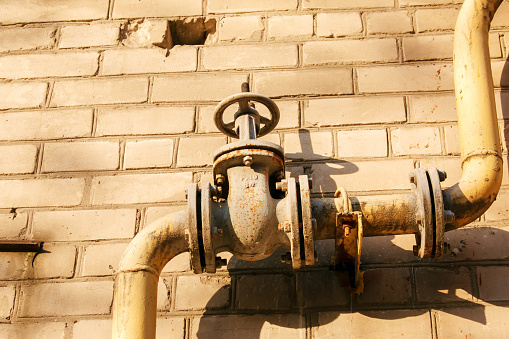 Rusty old gas tap on the background of the wall of the house.