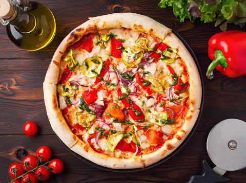 Vegan pizza with vegetables and pesto sauce on a wooden background. Gluten-free pizza with zucchini, red pepper, purple onion, cheese. Menu of cafes, pizzeria, restaurant. Close up. Copy space. Fresh