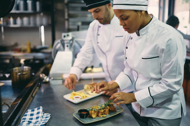 istock Black female chef and her colleague serving food while working at restaurant kitchen. 1394053747