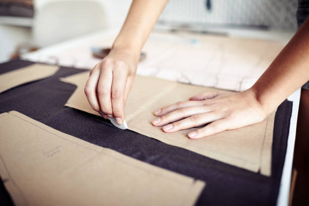 Seamstress Outlining Cardboard Pattern Hands of seamstress using chalk to outline cardboard sewing pattern on fabric when working in atelier clothing pattern stock pictures, royalty-free photos & images