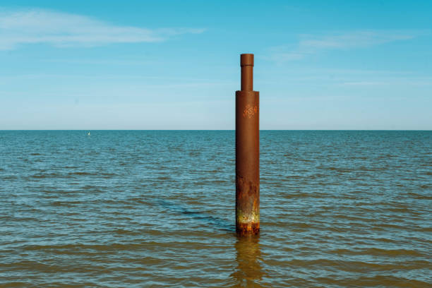 Large rusty steel construction pillar in blue sea with calm waves. Vertical abandoned building part, construction site near coastline. Ecology and recycling concep.t Large rusty steel construction pillar in blue sea with calm waves. Vertical abandoned building part, construction site near coastline. Ecology and recycling concept rusty pole stock pictures, royalty-free photos & images