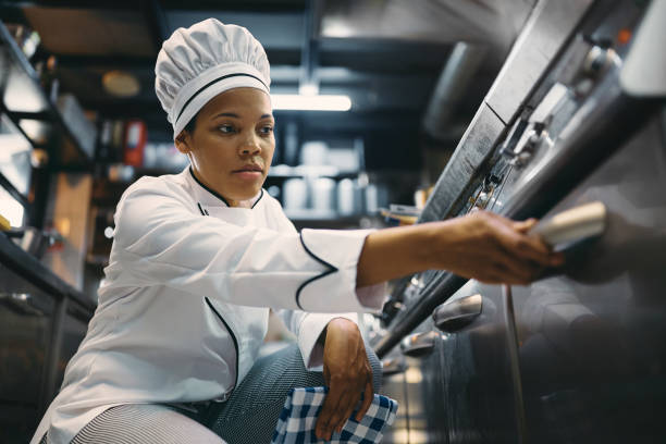 istock Black female professional cook using oven while preparing food at restaurant kitchen. 1394055831