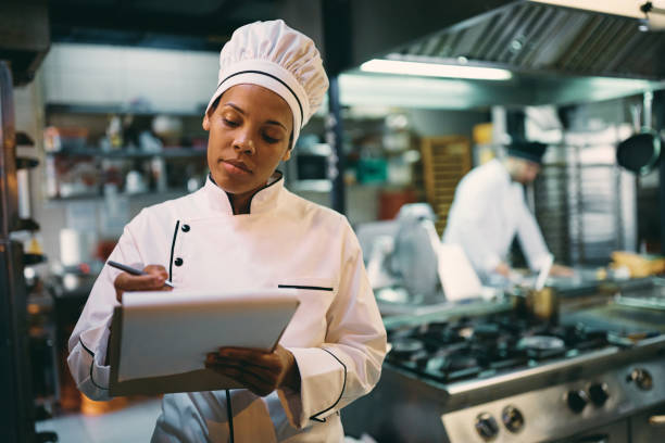 istock Black female chef going through checklist while working in the kitchen at restaurant. 1394056650