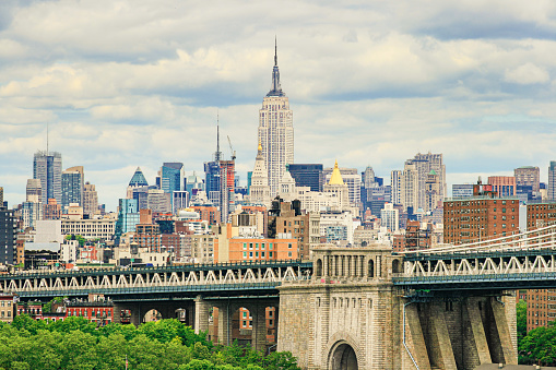 New York City Skyline with Empire State Building and Midtown Manhattan Skyscrapers, with Fragment of the Manhattan Bridge in the Foreground,\n NY, USA. Blue Sky with Puffy Clouds is in Background.