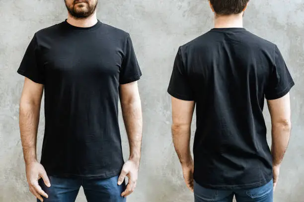 Young man with a beard in an empty black casual t-shirt. Front and rear view on a background of light gray concrete wall. Men's t-shirt template design and layout for print.