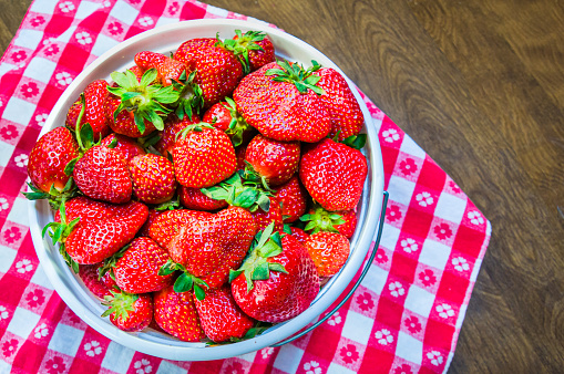 Freshly picked ripe strawberries in a white pail on a red checkered table cloth