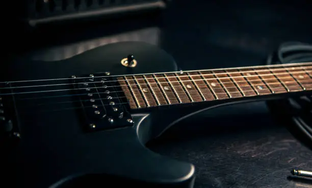 Photo of Close-up, black electric guitar on a dark background.